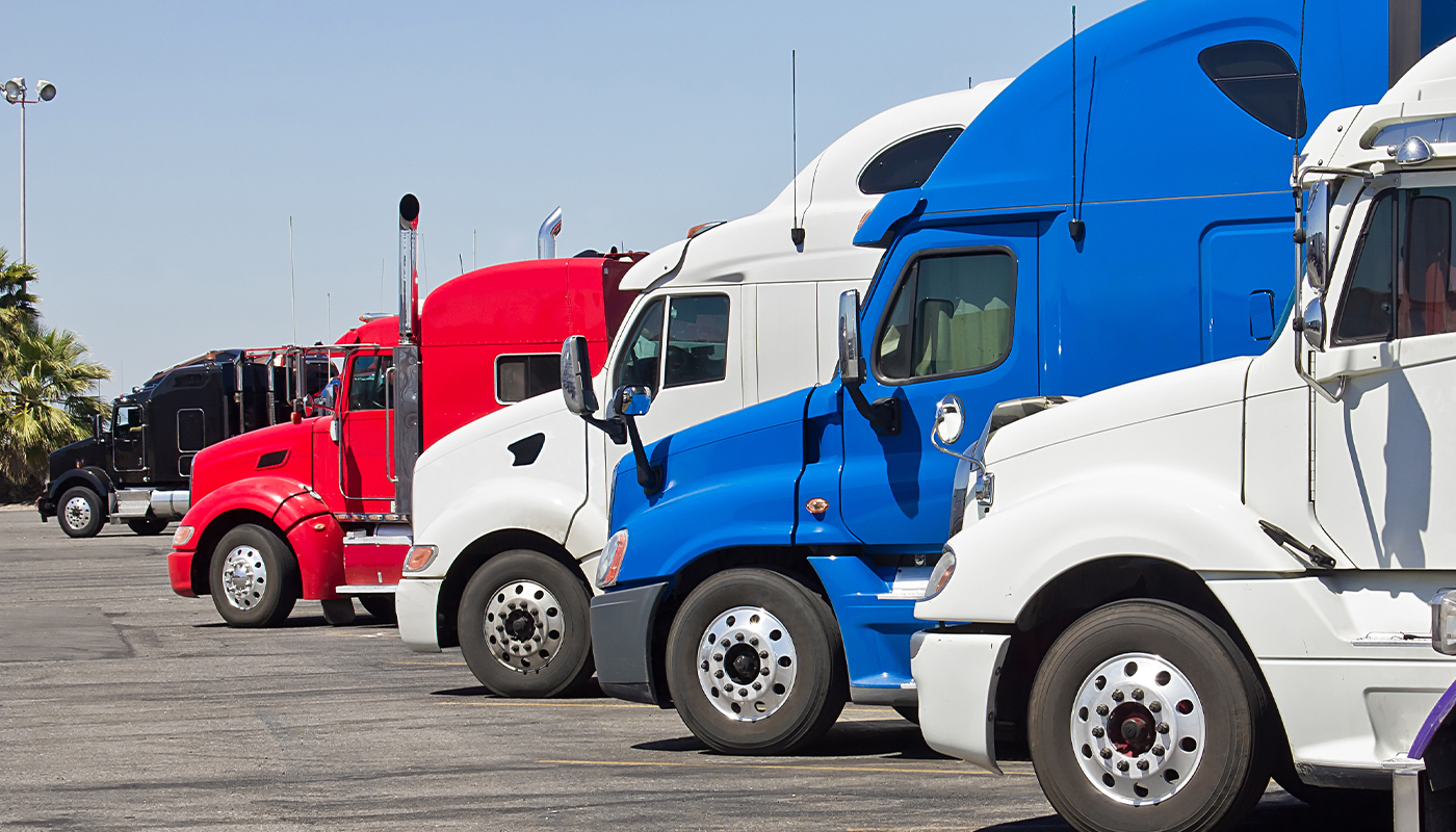 Five semi trucks lined up in a parking lot