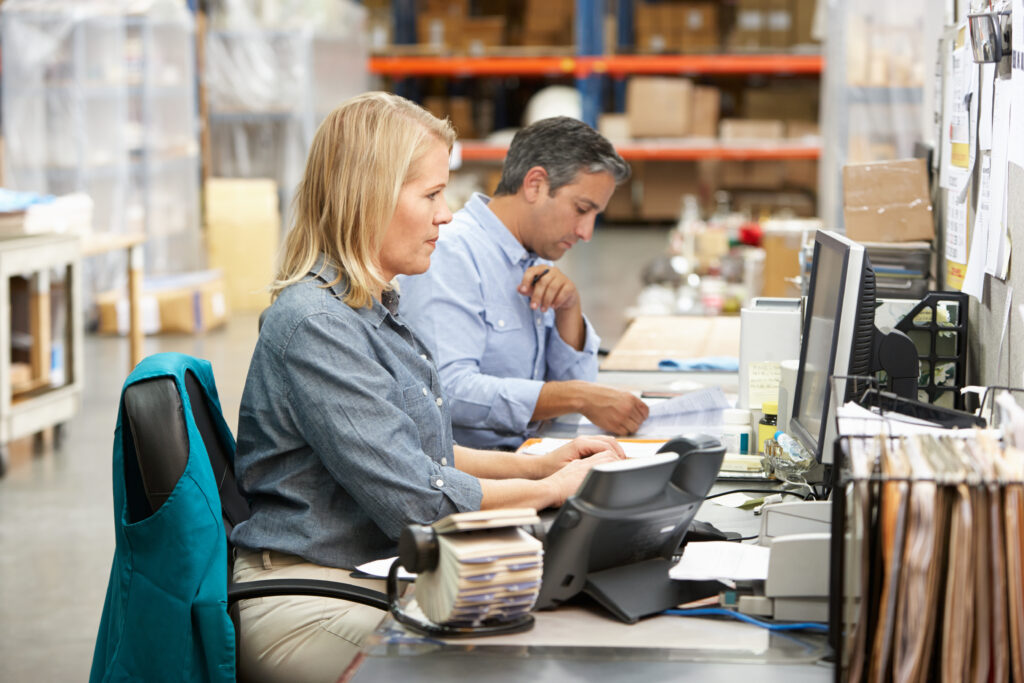 Two employees, female and male, working side-by-side a computers stationed on a warehouse using managed logistics services from Spot